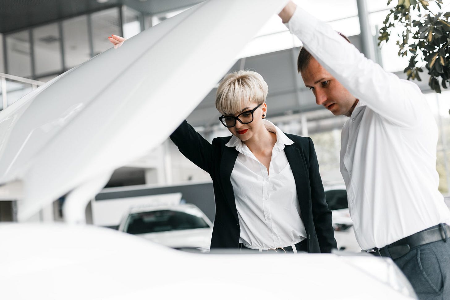 A couple at a dealership, looking under the hood of a car A couple at a dealership, looking under the hood of a car