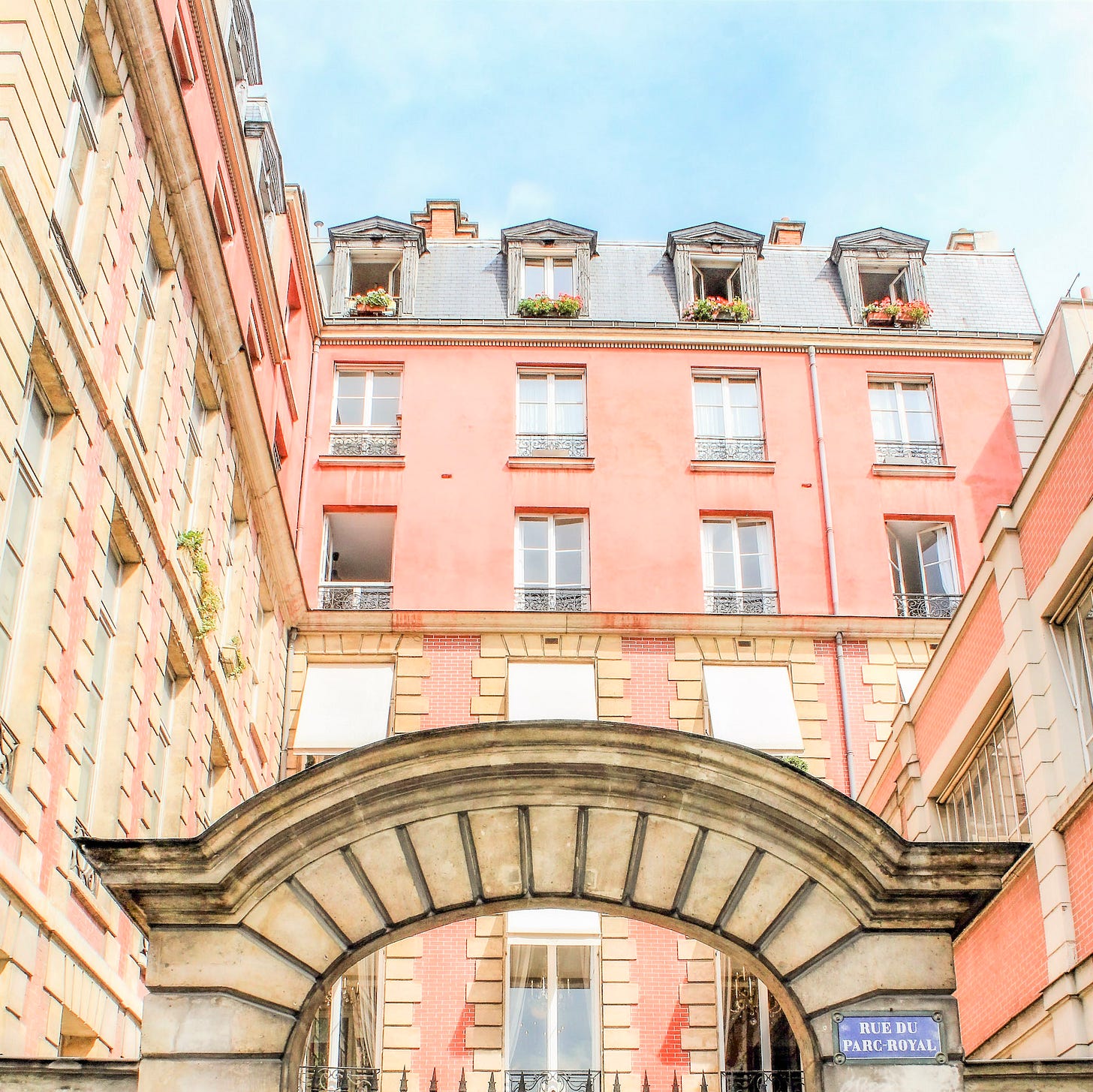 Pink and red brick architecture on Rue du Parc-Royal in the Marais, seen through a large stone archway.