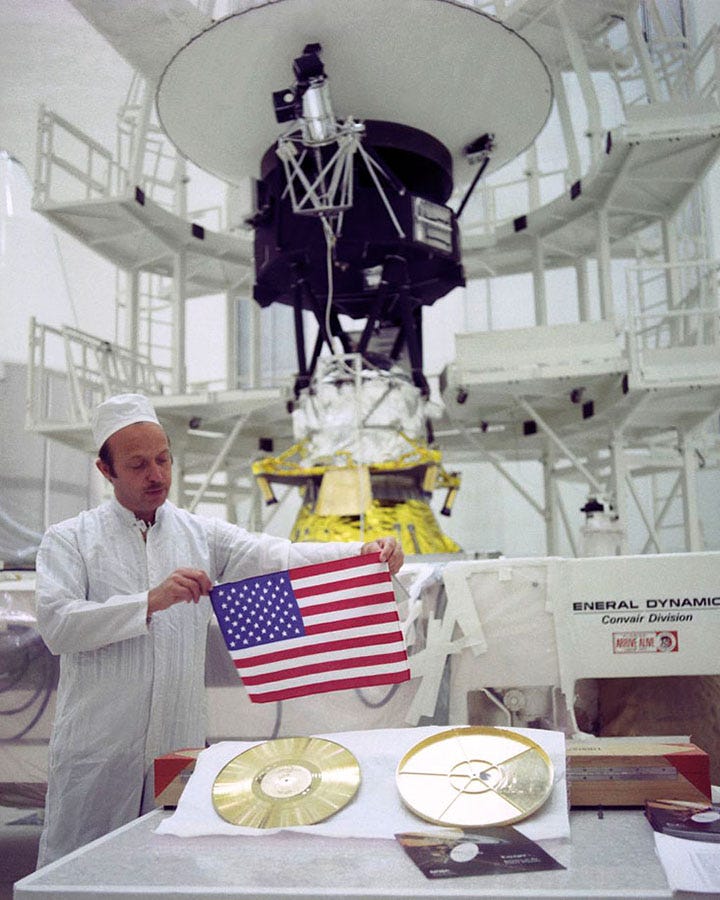 technician holding u.s. flag with voyager spacecraft in background technician holding u.s. flag with voyager spacecraft in background