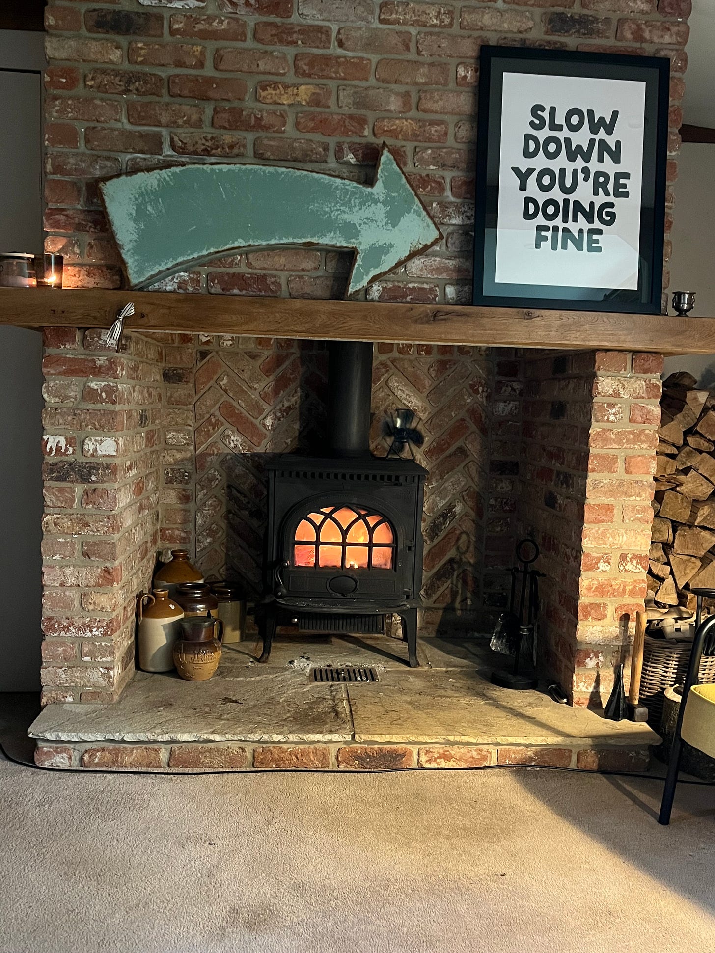 The snug room in the Timber House has the best two signs placed on the wooden mantle set into its red brick chimney breast. A large painted curved arrow points to a printed sign to its right, which reads: ‘Slow down, you’re doing fine.” Inside the hearth the bricks are set in a herringbone pattern and a fire blazes in a black iron wood burner placed on the hearth.