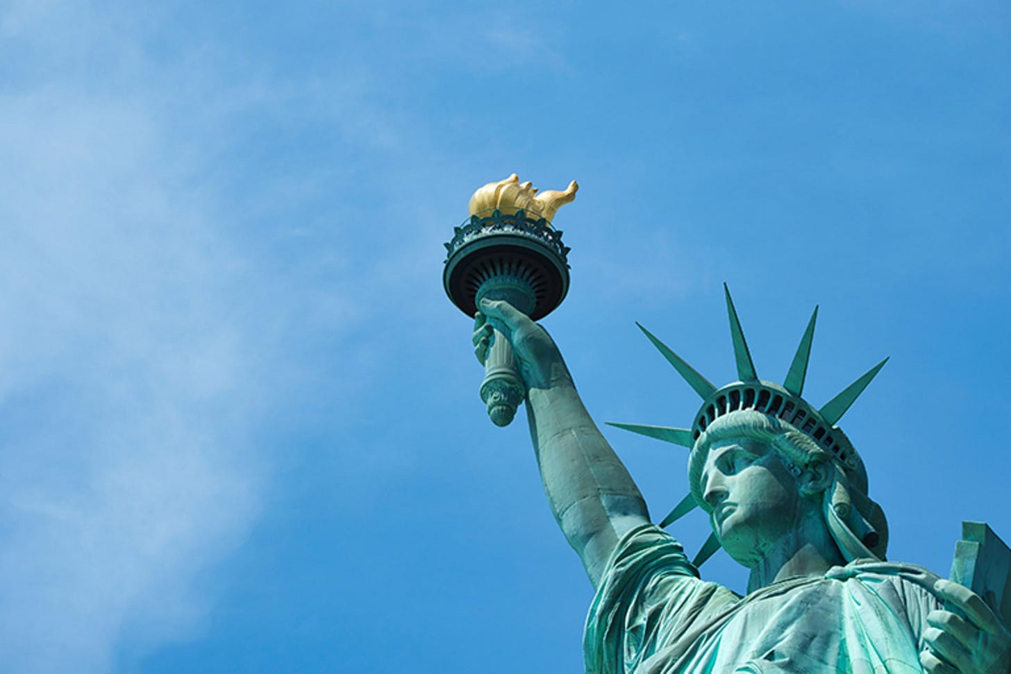 A close up shot of the Statue of Liberty underneath a blue sky.
