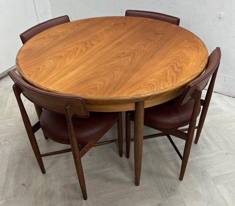 May include: A round wooden dining table with a visible grain pattern, accompanied by four matching chairs. Each chair features a wooden frame and a dark burgundy upholstered seat and backrest, arranged neatly around the circular table surface.