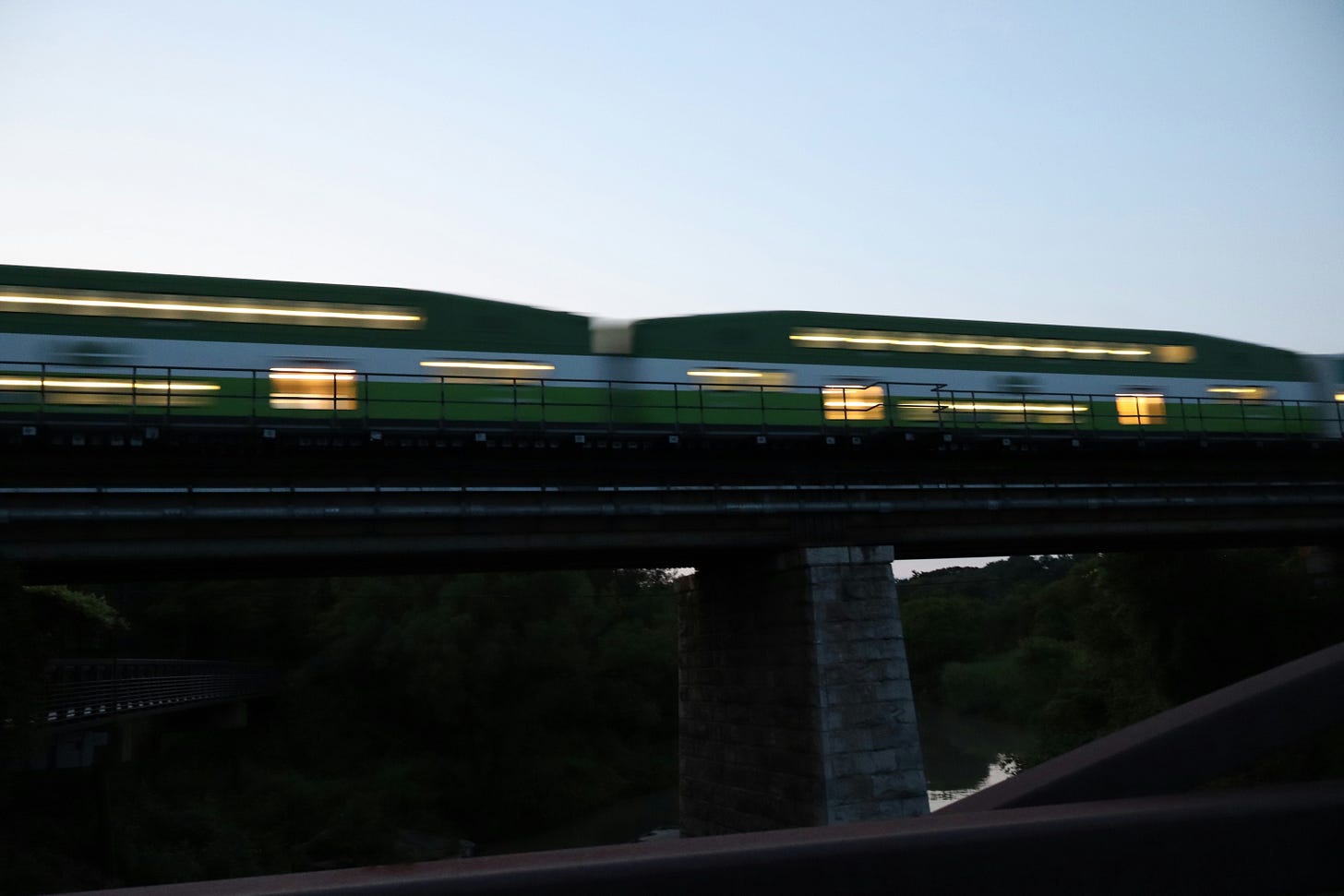 A green train traveling down train tracks next to a bridge