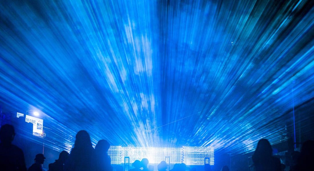 A bright blue shining light with a crowd of people in front of it A bright blue shining light with a crowd of people in front of it