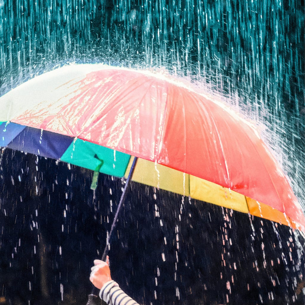 Photo of a rainbow umbrella being held up in the rain.