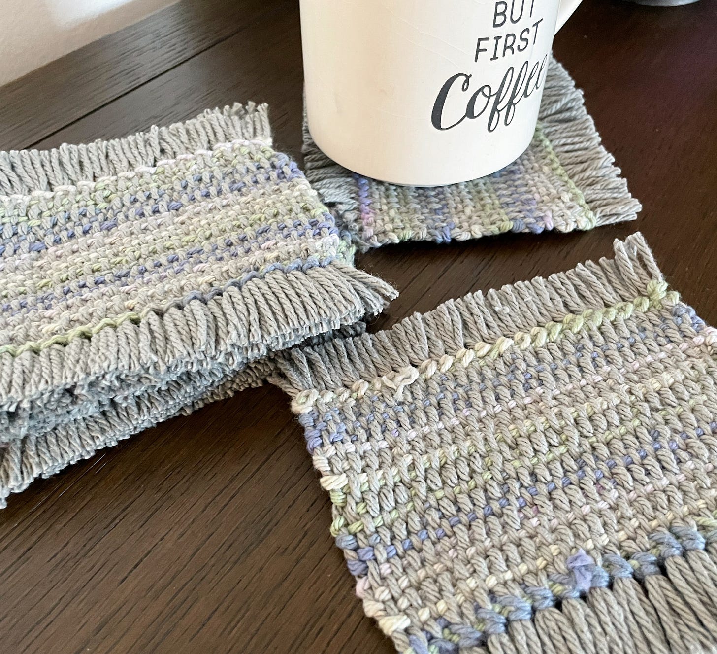 A stack of mug rugs on the left, one in the back with a mug on it, one in the front. Gray and muted colors. No diamonds.