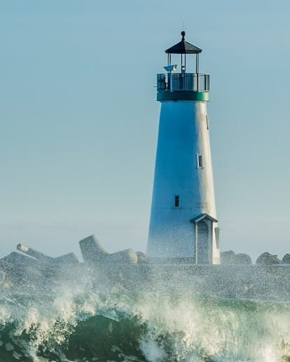 concrete lighthouse near rocks and ocean wave at daytime