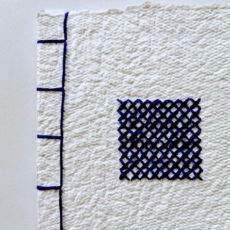 Handmade paper notebook bound using Japanese stab binding method with blue cross stitched square centre.
