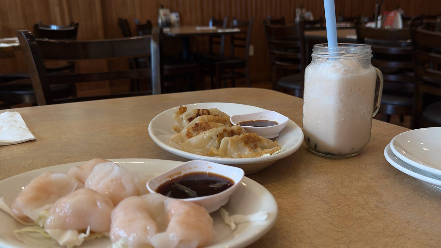Plated steamed shrimp dumplings, fried pot stickers, and a Strawberry Mango Bubble Tea with light blue straw.