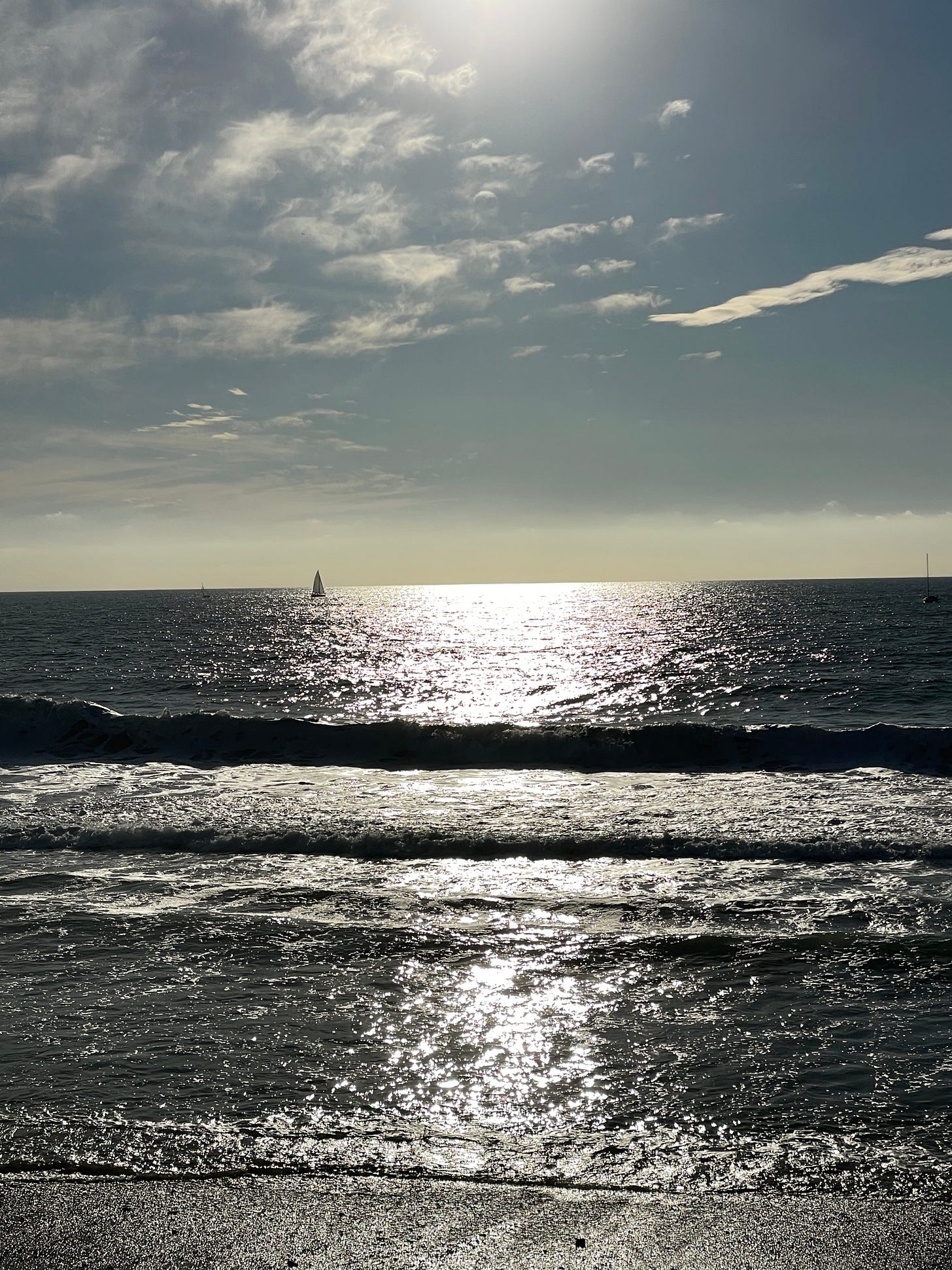 Landscape of ocean horizon mid-day with sailboat in the distance.