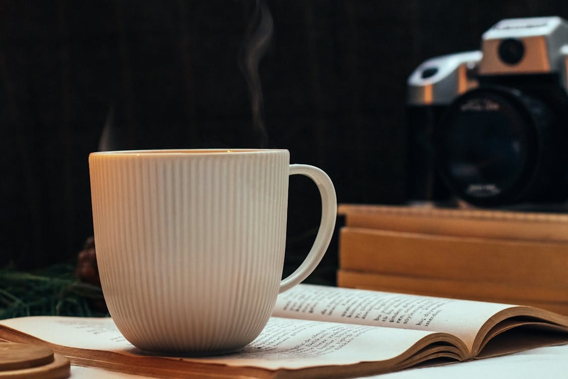 Free A steaming coffee mug rests on an open book, creating a cozy reading nook ambiance. Stock Photo