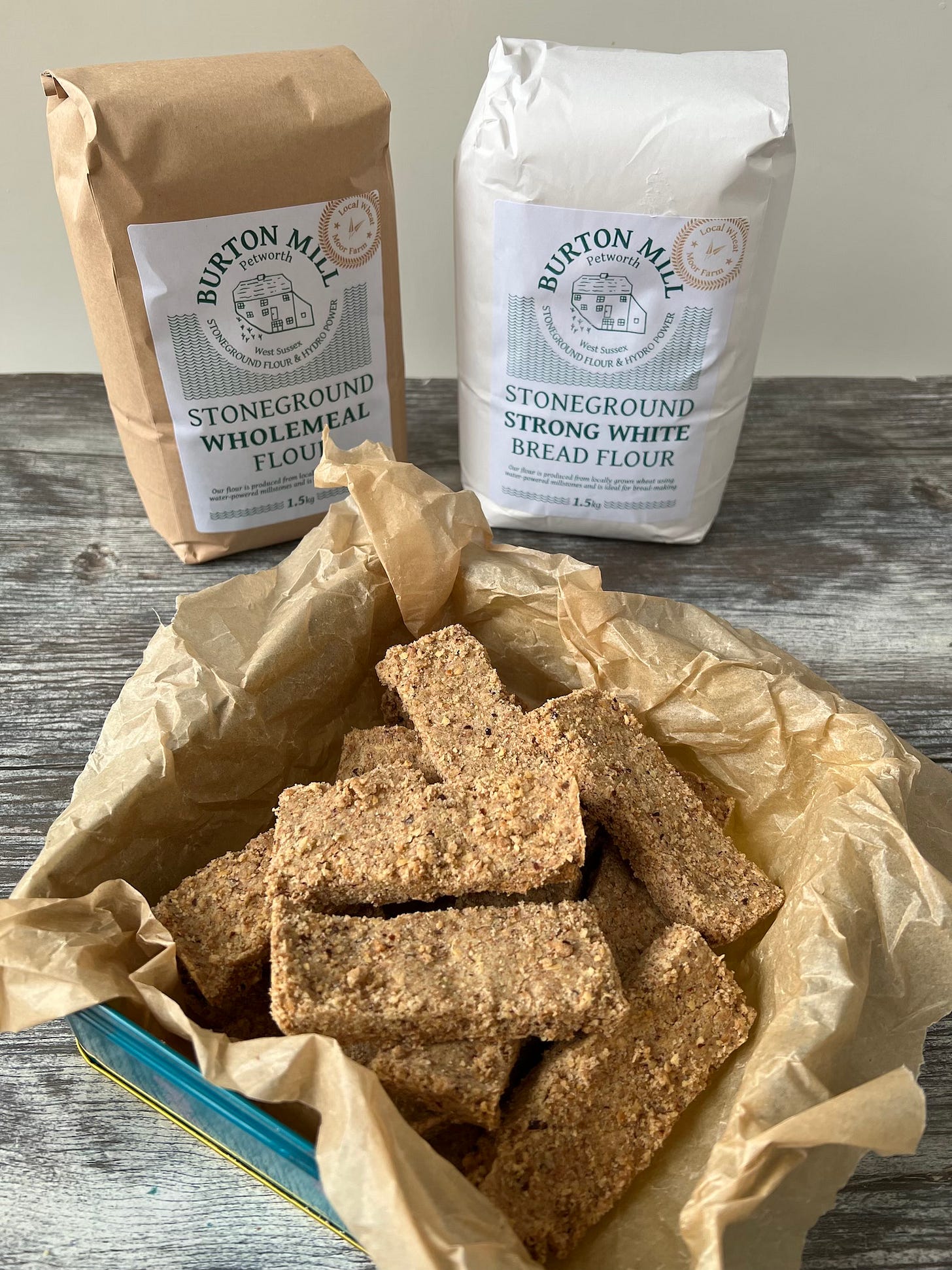short bread fingers in biscuit tin in front of two bags of flour