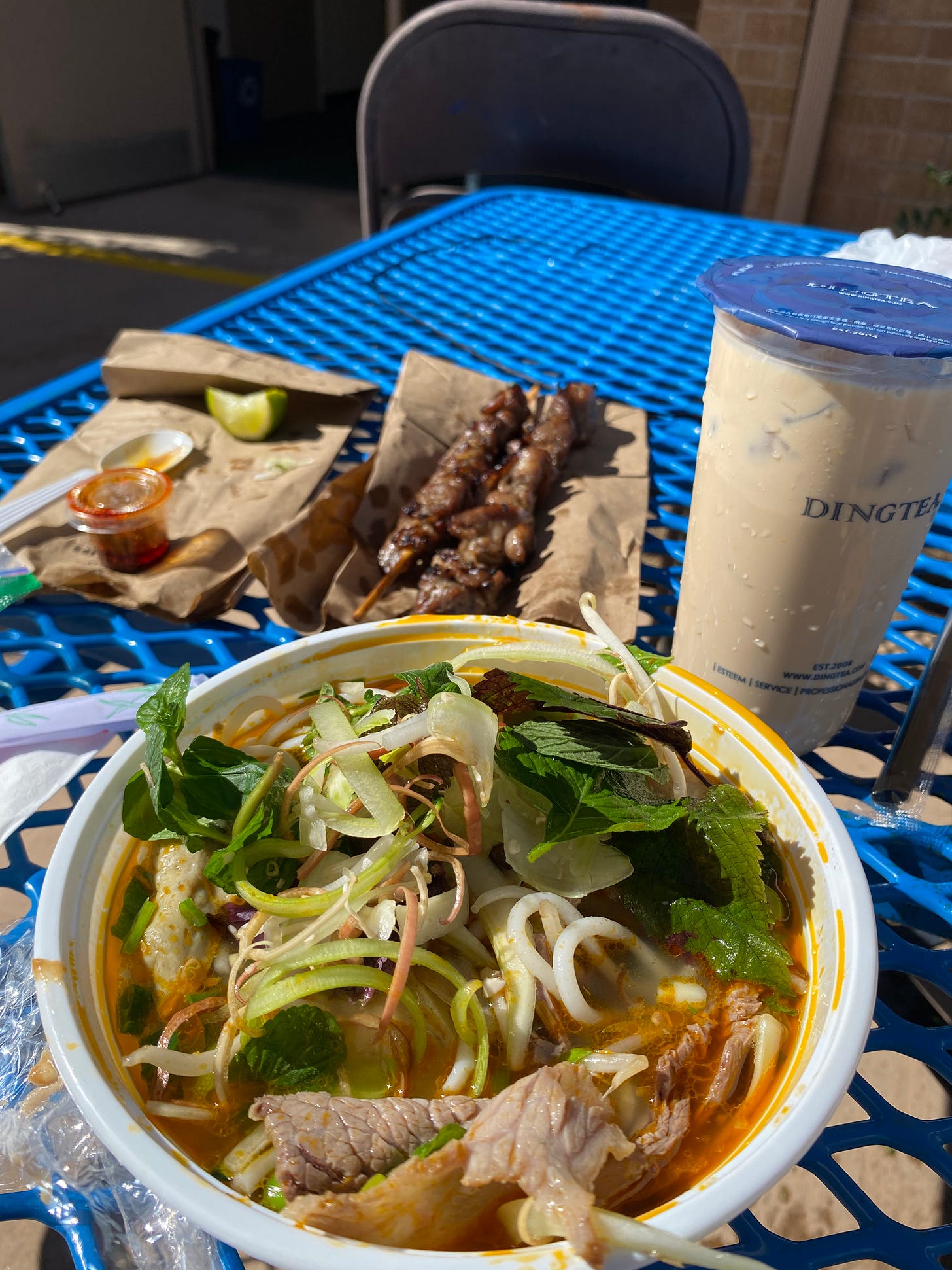 A blue table full of Vietnamese foods: skewers, pho, and boba tea.
