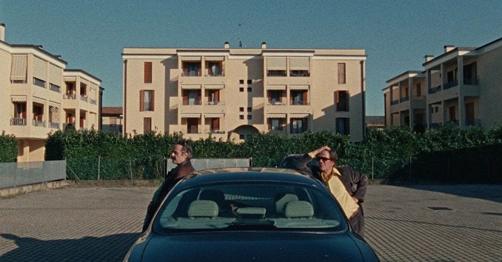  Carlobianchi e Doriano, due amici di bevute, si ritrovano a saltare di bar in bar in cerca del senso della vita nel film Le città di pianura di Francesco Sossai. Nel frame, i due amici sono appoggiati a un auto, parcheggiata tra le palazzine del Veneto.