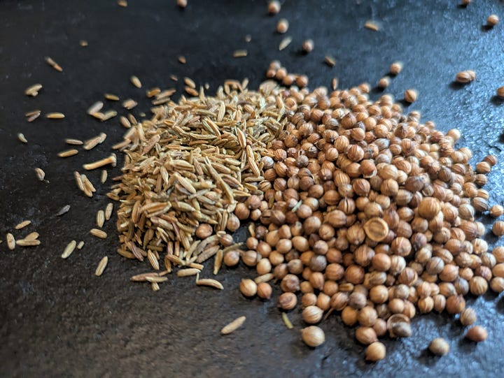 Whole coriander seeds and cumin seeds being dry-roasted and lightly crushed.