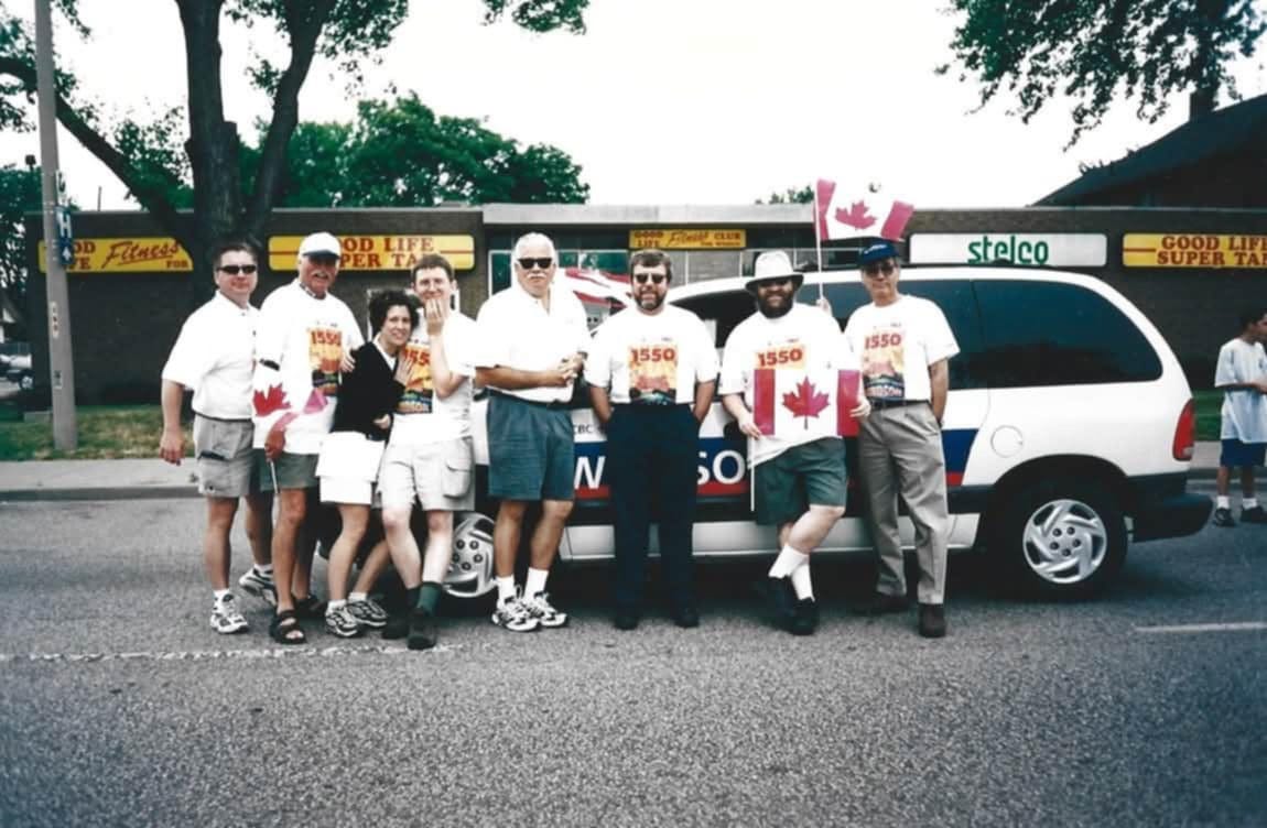 A 24-year-old group photo of a group of mostly middle-aged men wearing matching t-shirts advertising CBC Radio 1550 AM in Windsor. Near the middle of the pack is a 23-year old me with my arm around the woman who would later become my wife. We look sassy.