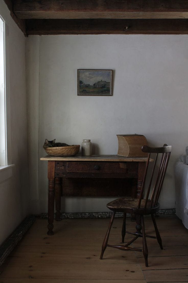 This may contain: an old desk and chair in a room with wooden floors, white walls and wood beams