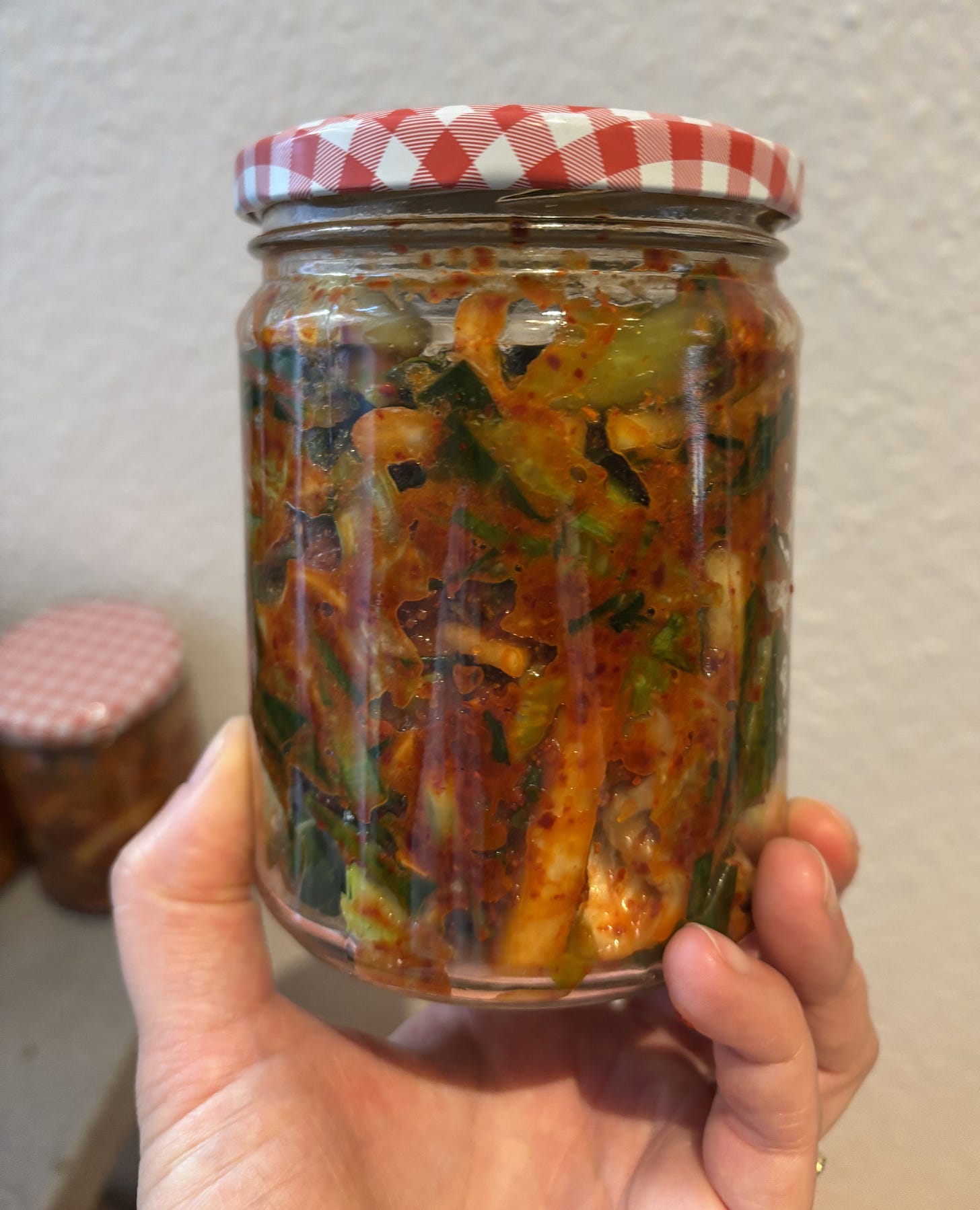 a hand holding a jar of red and green kimchi