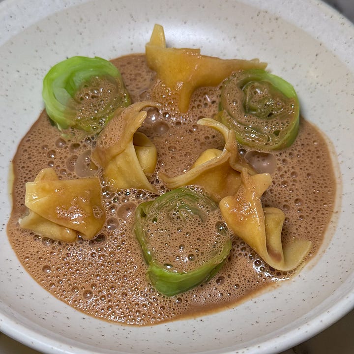  Langoustine cappelletti and rolled green cabbage in a frothy langoustine bisque with A whole dark stuffed morel beside a white asparagus spear, over amber jus and white-asparagus purée