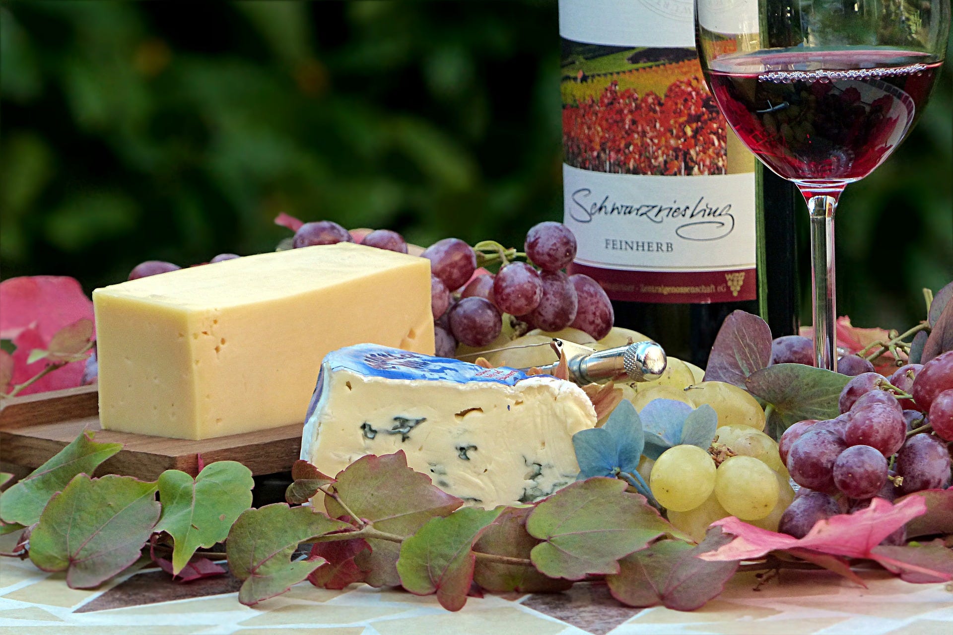 Table on which are set cheese, grape fruits, a glass of wine, and a bottle of wine