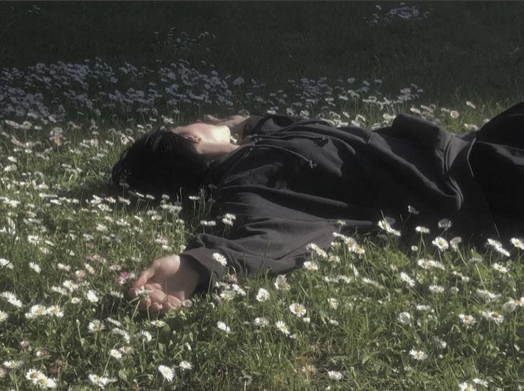 This may contain: a person laying in the grass with their head on his hands and eyes closed,