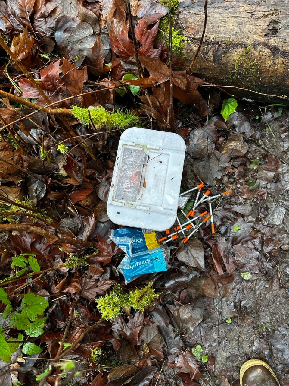 A plastic container with needles and a bag on the ground

Description automatically generated
