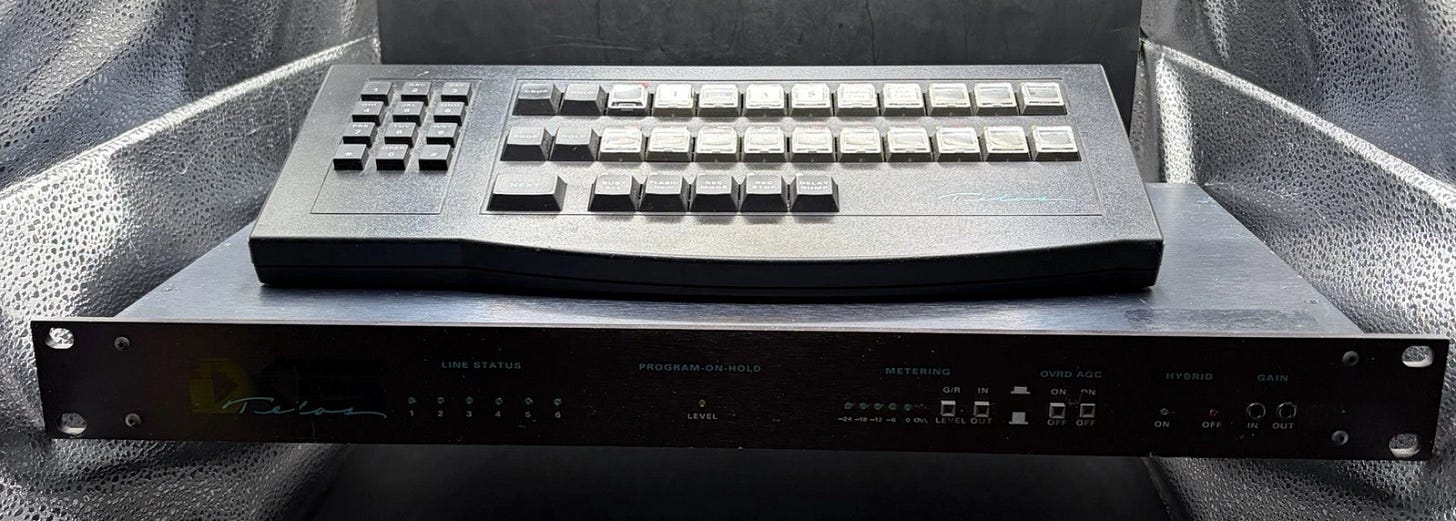 Black Telos ONE-X-SIX broadcast pod rack mount with multiple labeled buttons and silver front panel on a textured surface. Black Telos ONE-X-SIX broadcast pod rack mount with multiple labeled buttons and silver front panel on a textured surface.