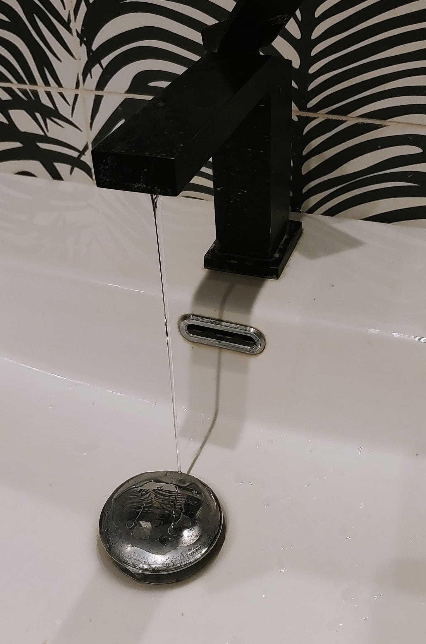 A very thin stream of water coming out of a black faucet over a white sink.