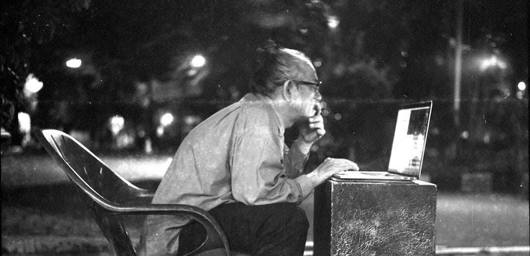 man sitting on chair infront of table while looking at laptop man sitting on chair infront of table while looking at laptop