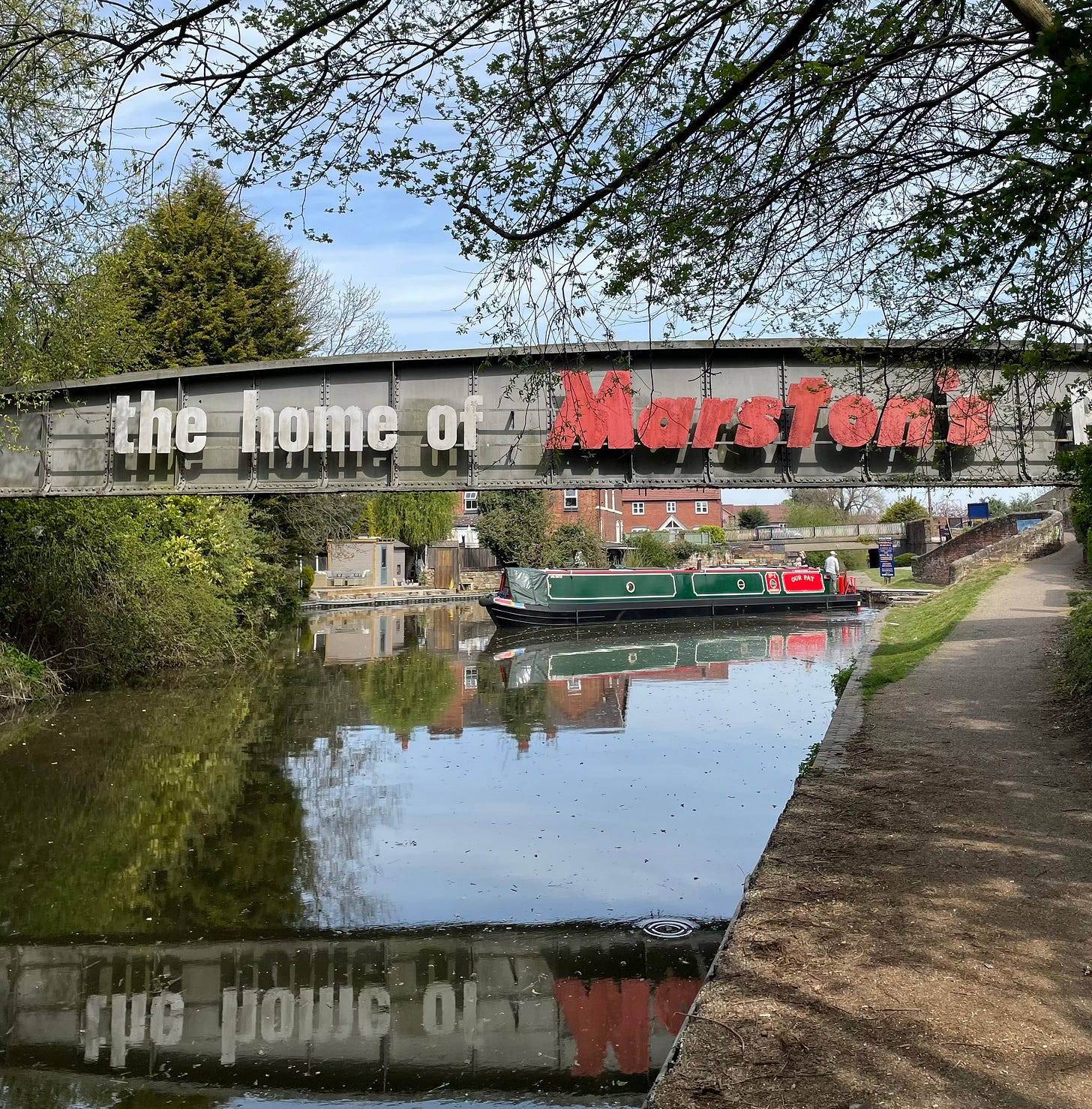 The canal at Burton. A bridge, bearing an advert for Marston's Brewery in the foreground and a canal boat in the background.