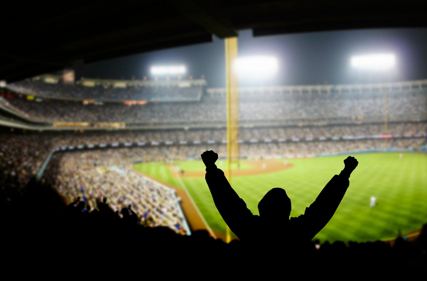 A fan, arm raised, cheering (or trying to start the wave) at a packed pro baseball game