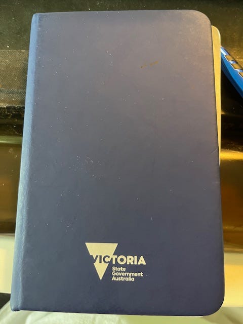 A closed blue notebook with the words "Victoria: State Government Australia" in white letters. A closed blue notebook with the words "Victoria: State Government Australia" in white letters.