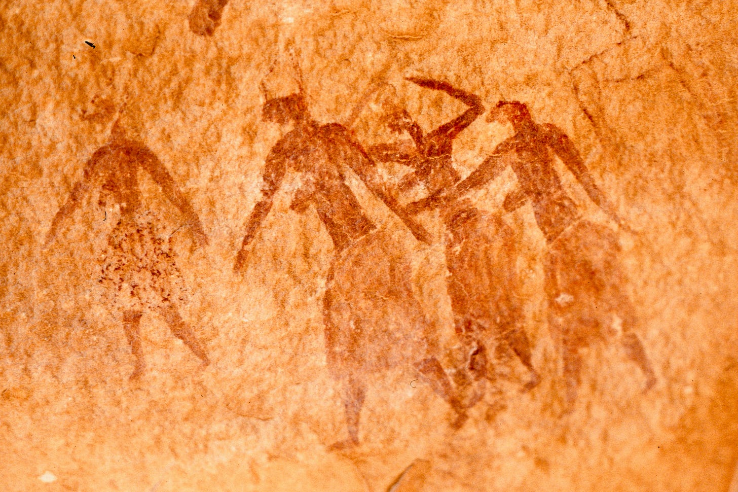 Prehistoric art on rough-textured, golden-colored rock showing several ochre-colored figures walking away