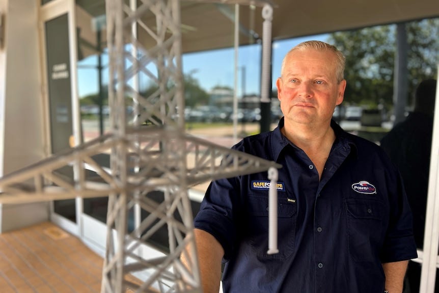 A man in a navy blue shirt stands in front of a model of a transmission tower