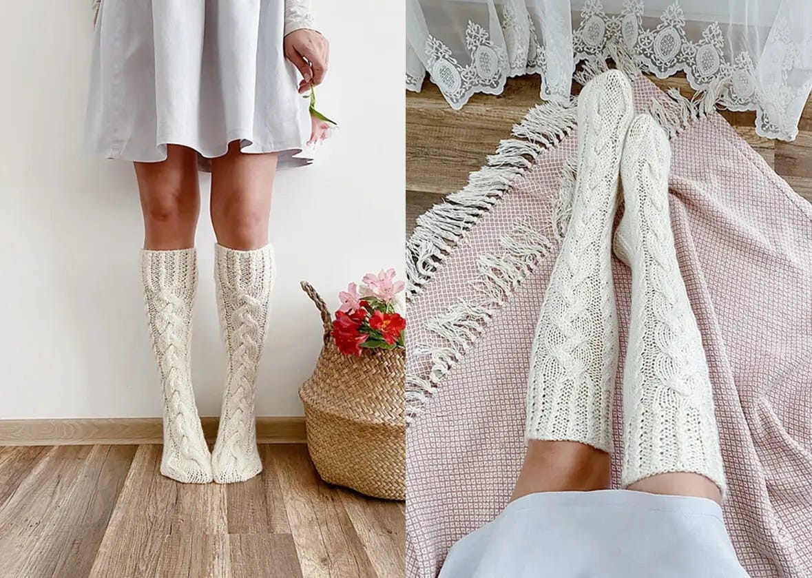 A woman stands next to a woven basket with flowers, wearing white knee-high socks with cables and a white dress.