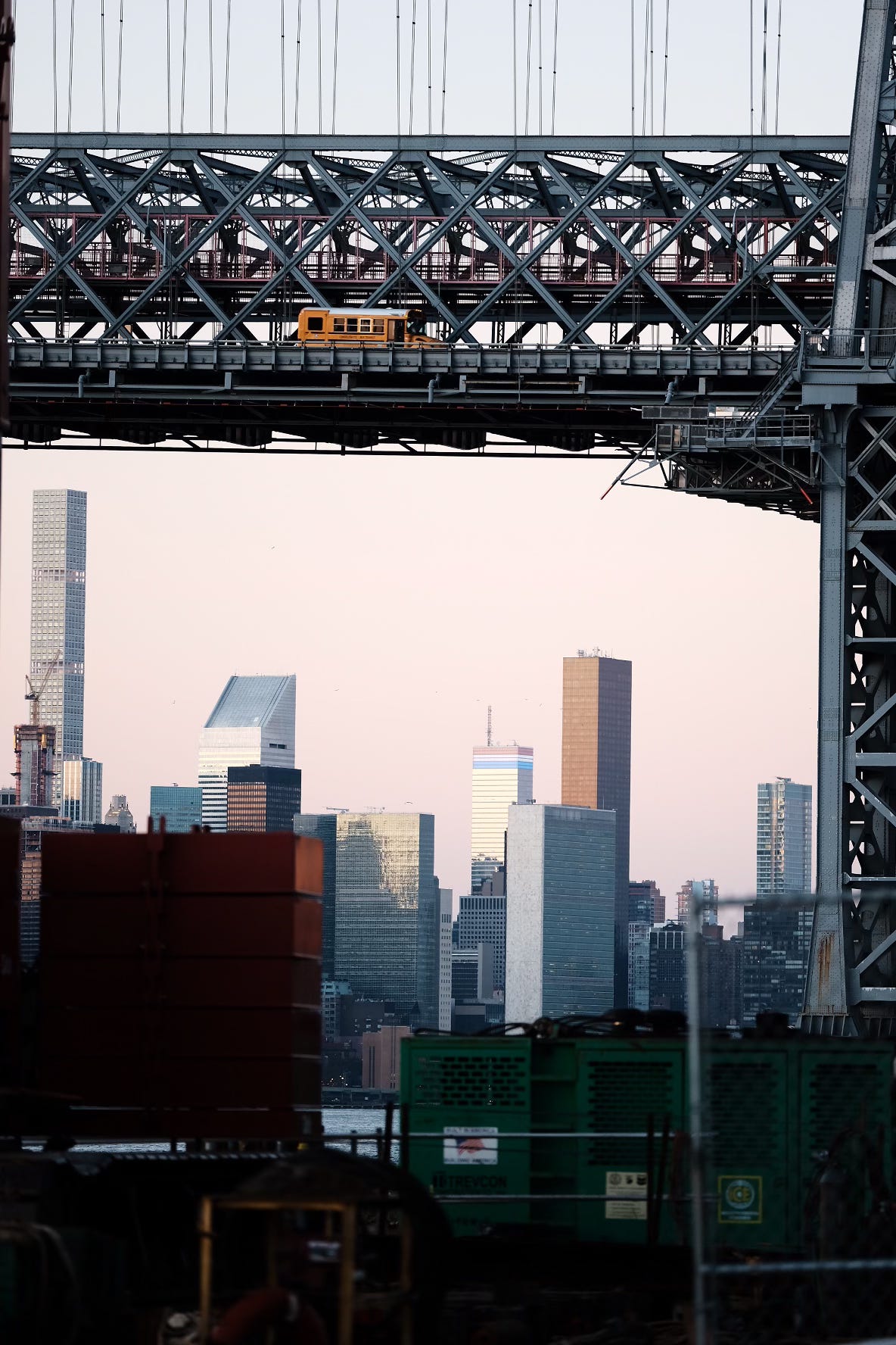 Yellow school bus crossing the Williamsburg Bridge with the Manhattan skyline behind, photographed from a nearby vantage point