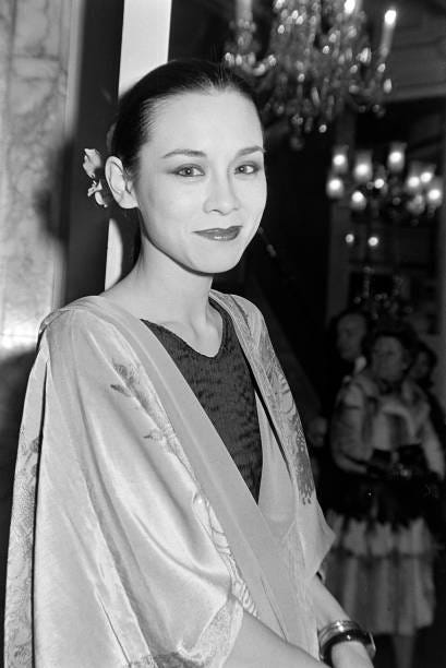 A close-up imahe of a smiling young woman wearing a black pleated dress beneath a lighter stenciled velvet cloak.