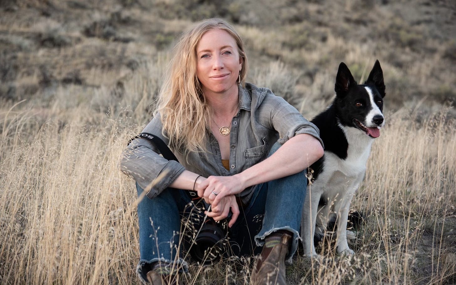 woman sitting in tall grass with black and white dog