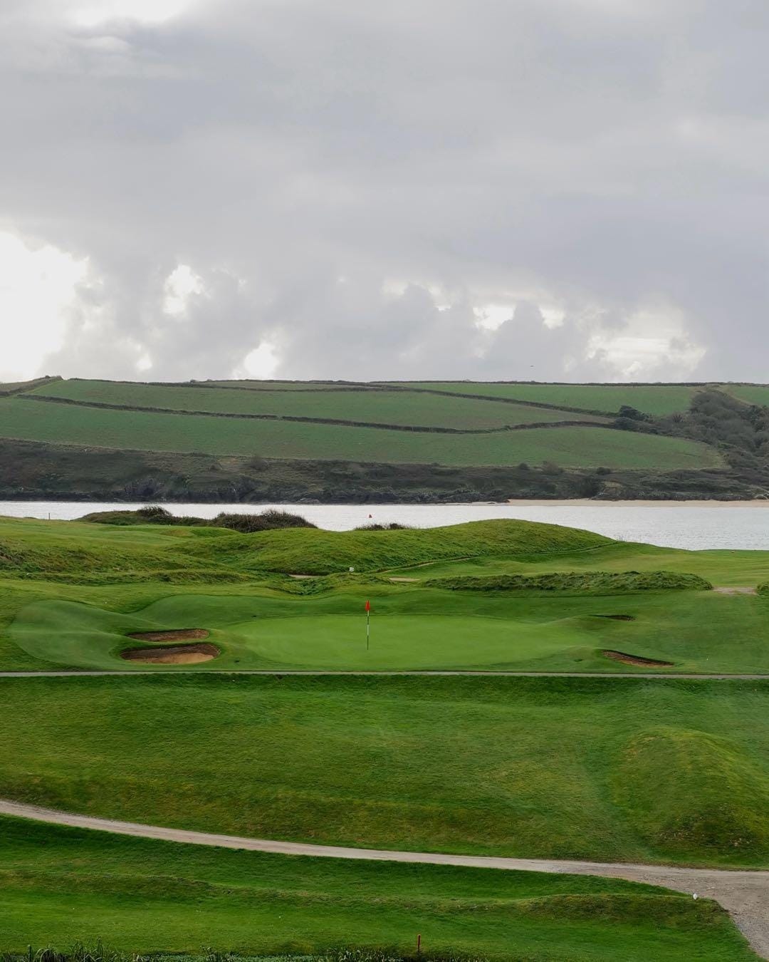 A golf course with a body of water and a cloudy sky

Description automatically generated