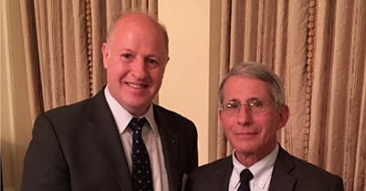 Peter Daszak of EcoHealth Alliance and Dr. Anthony Fauci pose together in formal attire in front of gold curtains. 