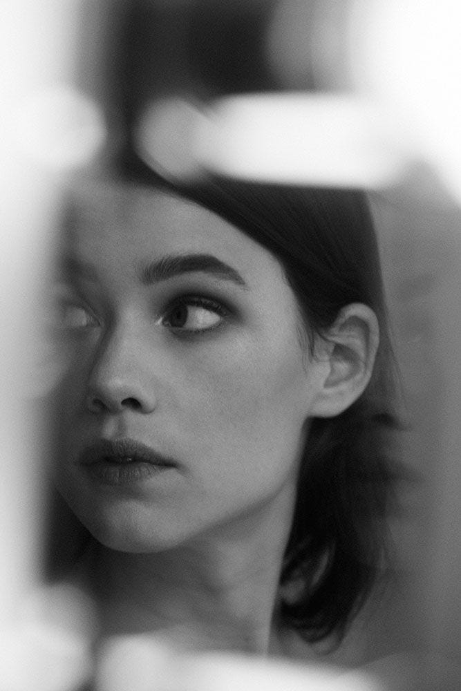 This may contain: a black and white photo of a woman looking at herself in the mirror with her eyes closed