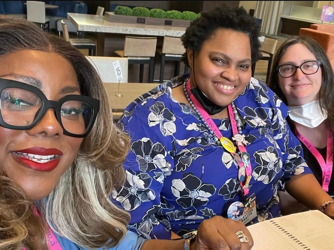 Photo of Tati Richardson, a Black woman with black glasses and red lipstick; Celestine Martin, a Black woman wearing a blue floral-patterned shirt and a lanyard decorated in pins; and me, a white woman wearing black glasses and the smug smile of someone whose lunch was $7.00 exactly