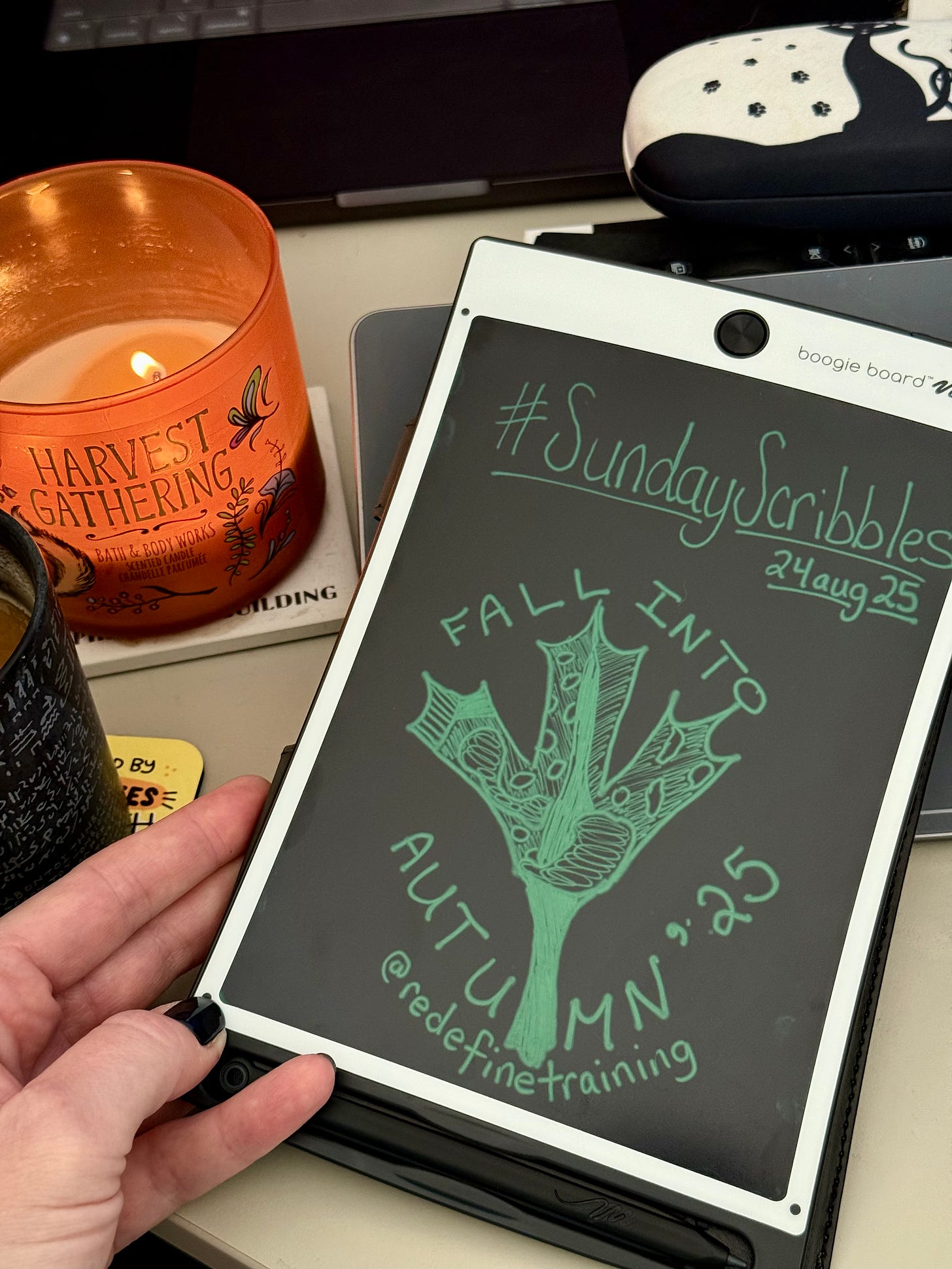 A digital sketch by Georgina Dean on a white Boogie Board. The sketch shows a large, green maple leaf with detailed veins. The text reads "#SundayScribbles, 24aug25, FALL INTO AUTUMN '25," and "@redefinetraining." A lit candle is visible in the background.
