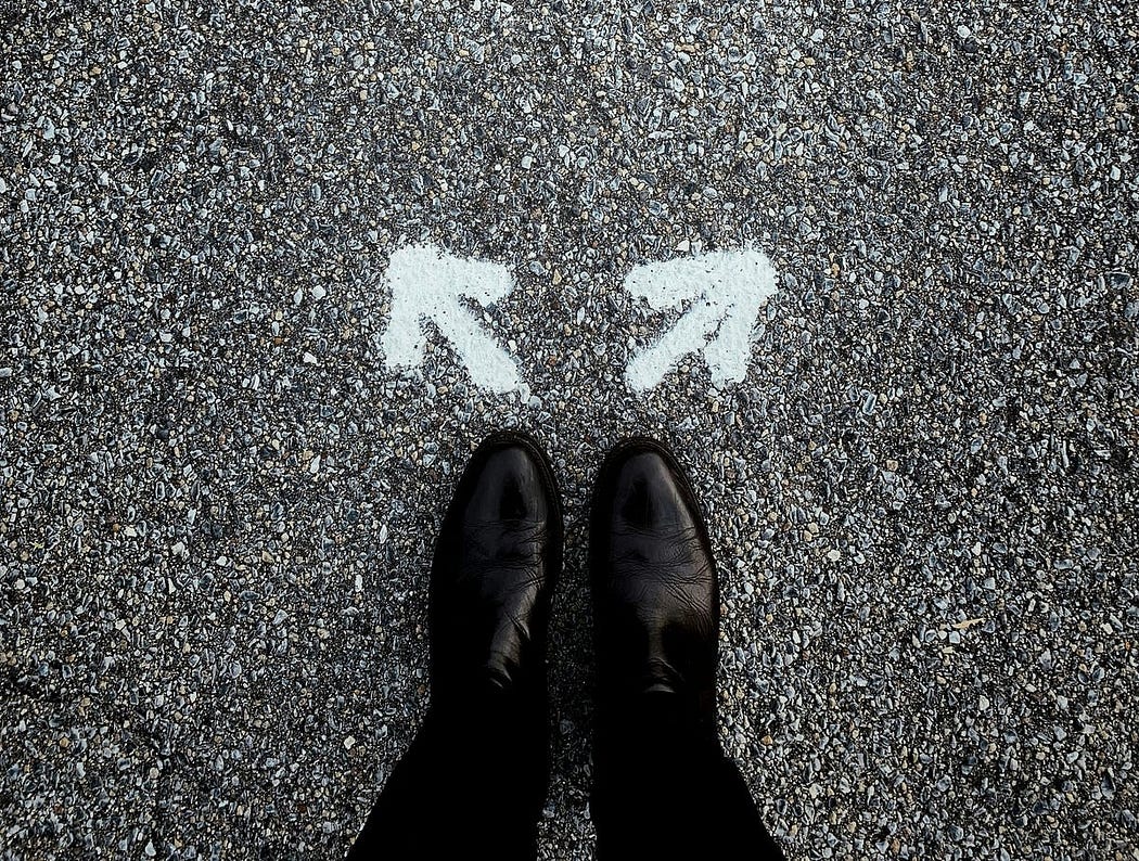 Standing in the road in black boats with opposite direction arrows drawn on the ground.