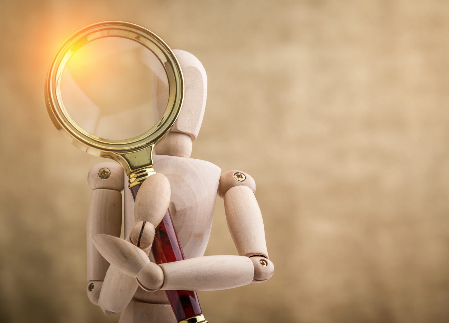 A wooden artist’s mannequin holding up a magnifying glass, with sunlight glinting off the metal rim, symbolizing introspection and the search for meaning.