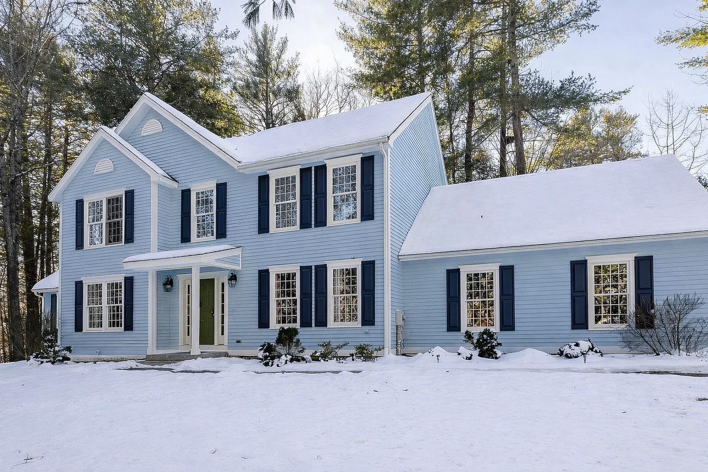 Light blue colonial-style home in New Hampshire with dark blue shutters and snow on the ground.
