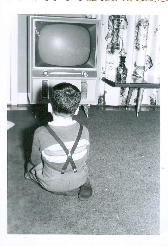 A vintage photograph from the 1950s of a young boy facing away from the camera, looking at a blank television. A vintage photograph from the 1950s of a young boy facing away from the camera, looking at a blank television.