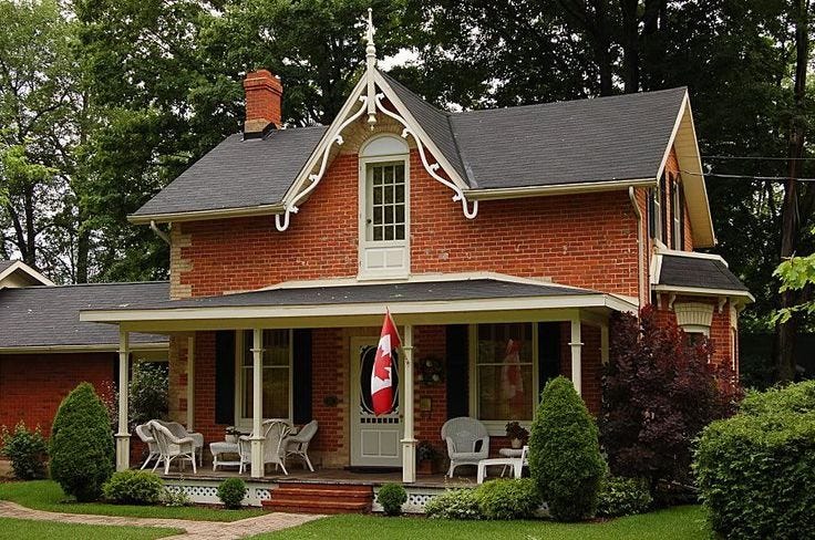 This may contain: a red brick house with two porches and chairs on the front lawn, surrounded by trees This may contain: a red brick house with two porches and chairs on the front lawn, surrounded by trees