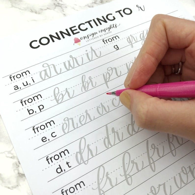 May include: A worksheet with the title "Connecting to r" and the text "ensign insights lettered by Sarah" printed on it. The worksheet is for practicing cursive handwriting and includes lines for writing letters from different starting points. A hand is shown writing on the worksheet with a pink pen.