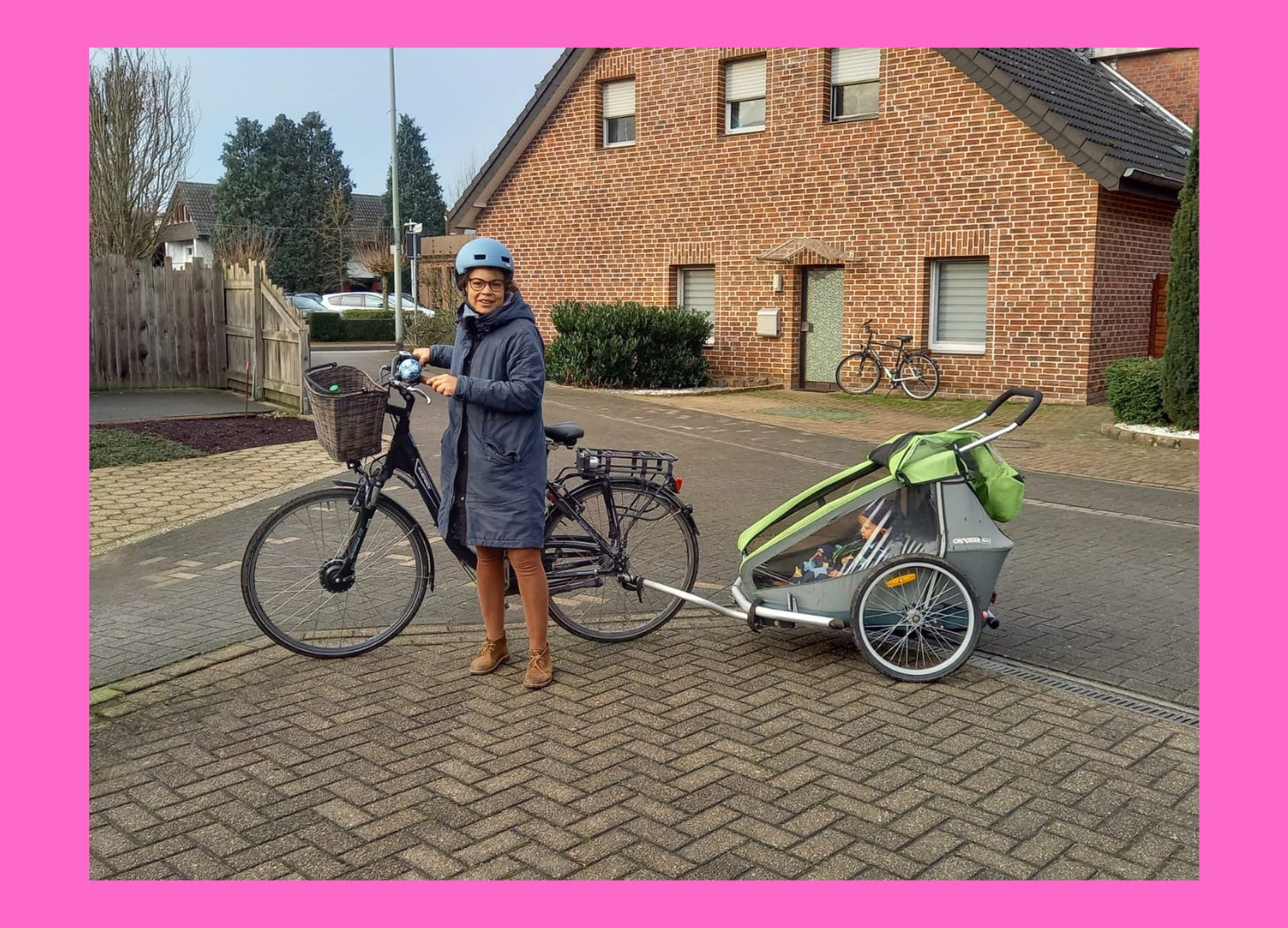 Photo of a woman in front of a bike with a bike trailer holding a small child.